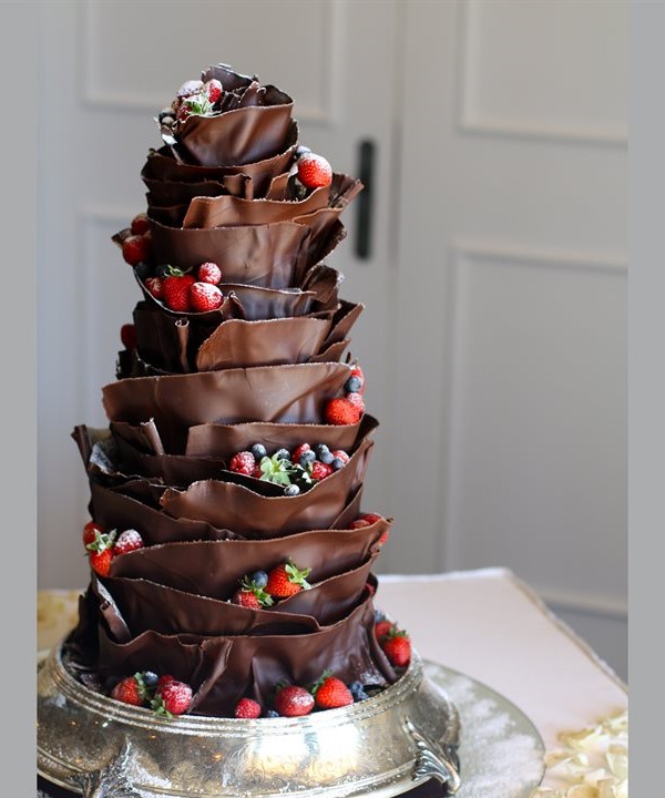 Tall multi-tier dark couverture chocolate wedding cake with sculpted ruffles, berries and silver pedestal